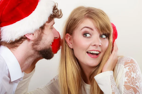 Man in santa hat whispering to woman ear. Stock Picture