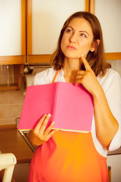 Housewife with cookbook in kitchen.