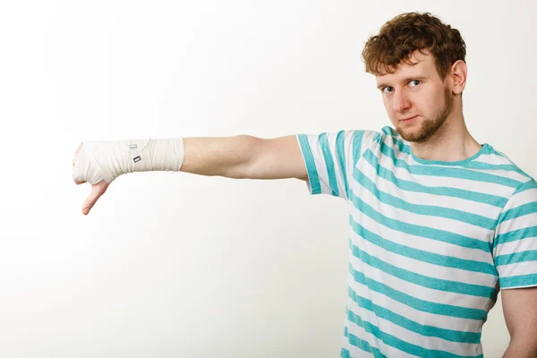 Sad man showing thumb down by bandaged hand. — Stock Photo, Image