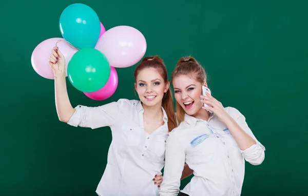 Two girls with mobile phone and balloons