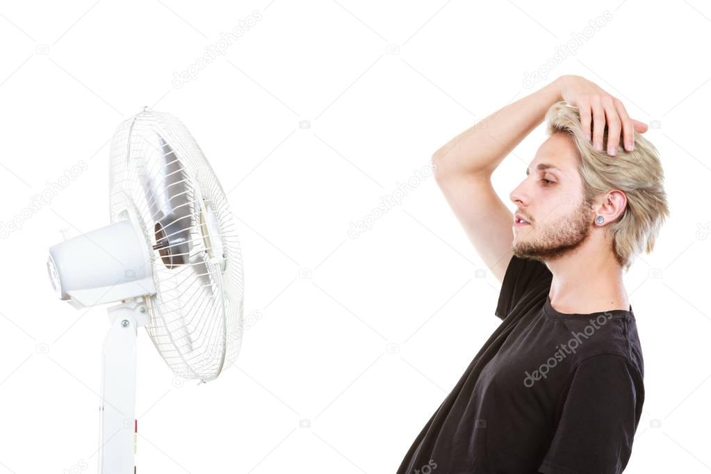 Young man fighting with wind from cooling fan