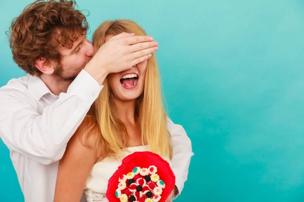 Hombre dando mujer caramelo manojo cubriendo sus ojos . — Foto de Stock