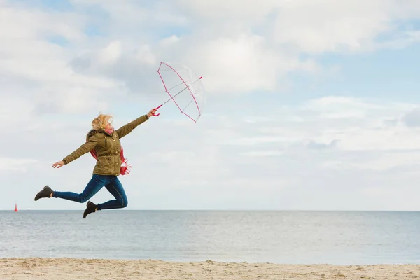 Woman jumping with transparent umbrella on beach — Stock Photo, Image