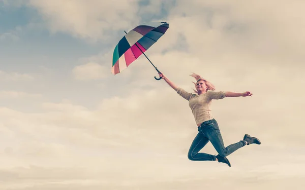 Woman jumping with colorful umbrella on beach — Stock Photo, Image
