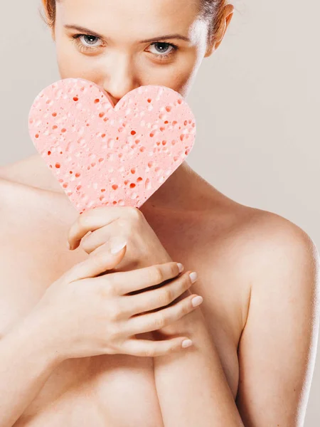 woman holding pink heart sponge in hands.