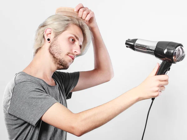 Молодой человек сушит волосы феном — стоковое фото