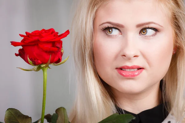 Kvinna med röd ros nära ansiktet ser melankolisk — Stockfoto