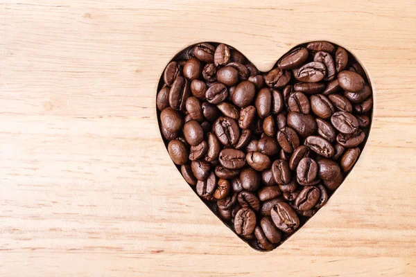 Kávová zrna na dřevěné desce ve tvaru srdce — Stock fotografie