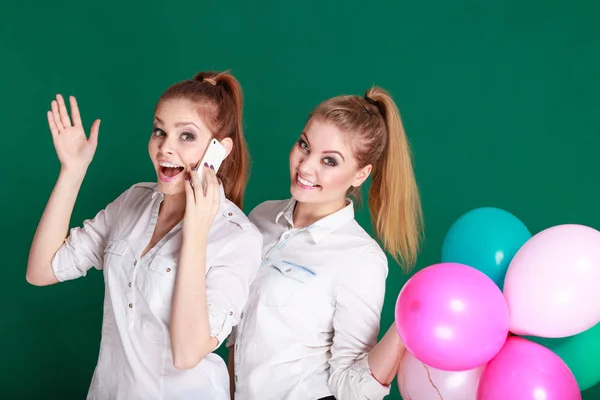 Duas meninas com telefone celular e balões — Fotografia de Stock