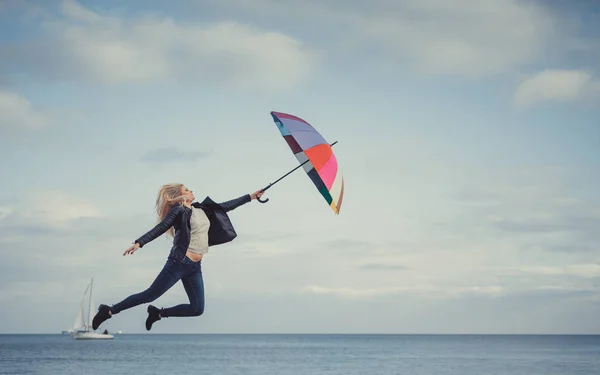 Woman jumping with colorful umbrella on beach — Stock Photo, Image