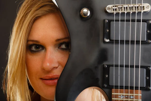 Blonde woman holding electric guitar, black background — Stock Photo, Image