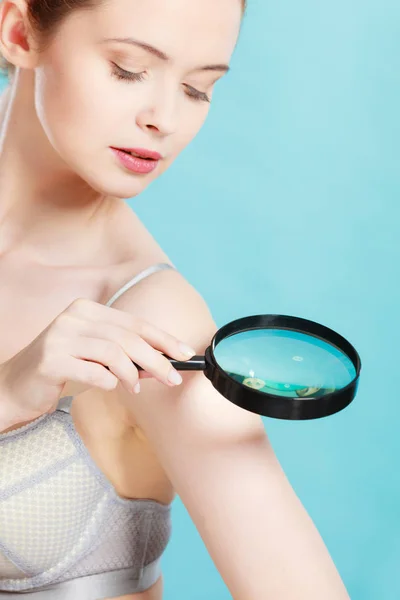 Woman using magnifying glass to examine her moles skin
