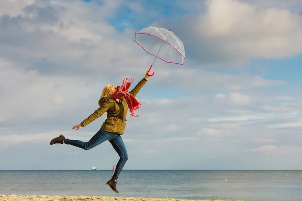 Woman jumping with transparent umbrella on beach — Stock Photo, Image