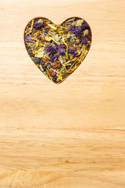 Dried herb leaves heart shaped on wooden surface — Stock Photo, Image