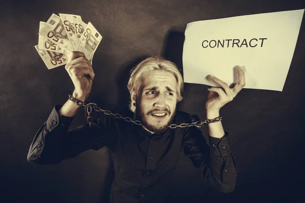 Man with chained hands holding contract and money