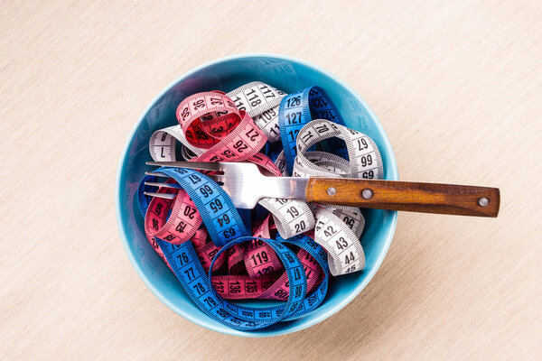 Many colorful measuring tapes in bowl on table
