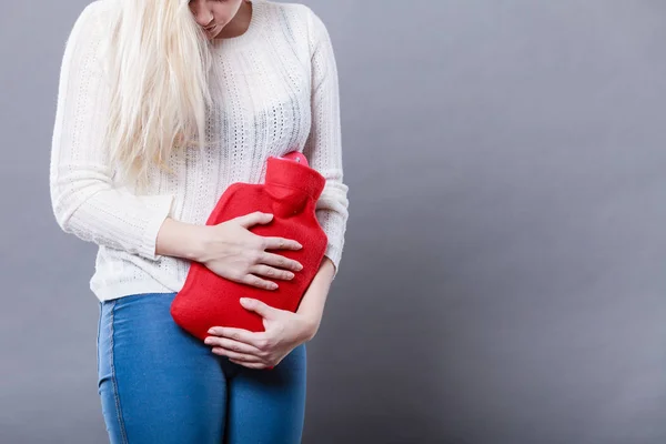 Woman feeling stomach cramps holding hot water bottle — Stock Photo, Image