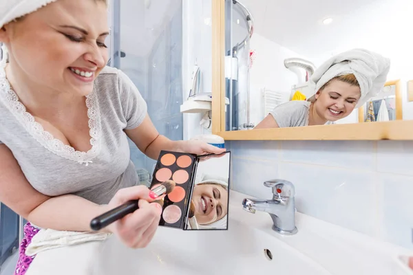 Woman in bathroom applying contour bronzer on brush
