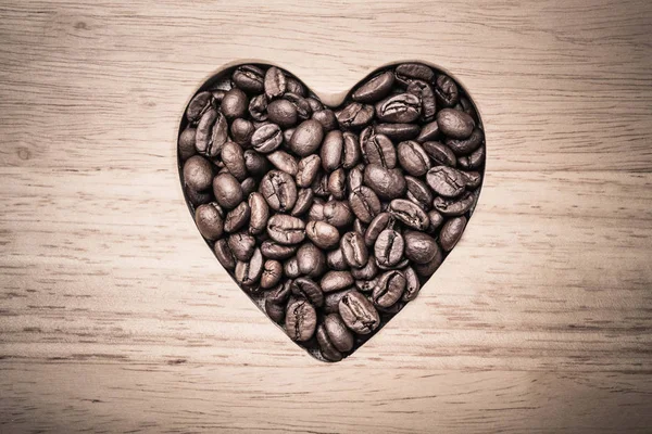 Grains de café en forme de coeur sur planche en bois — Photo