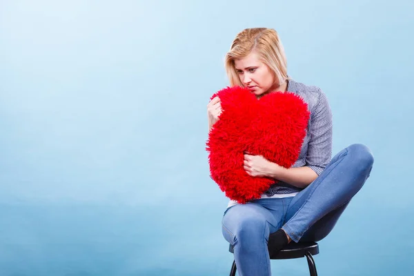 Mujer triste sosteniendo almohada roja en forma de corazón —  Fotos de Stock