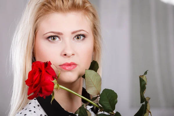 Kobieta trzyma red rose w pobliżu twarz patrząc melancholijny — Zdjęcie stockowe