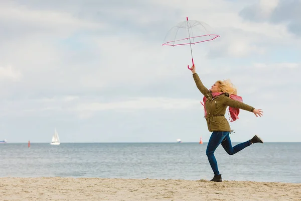 Woman jumping with transparent umbrella on beach — Stock Photo, Image