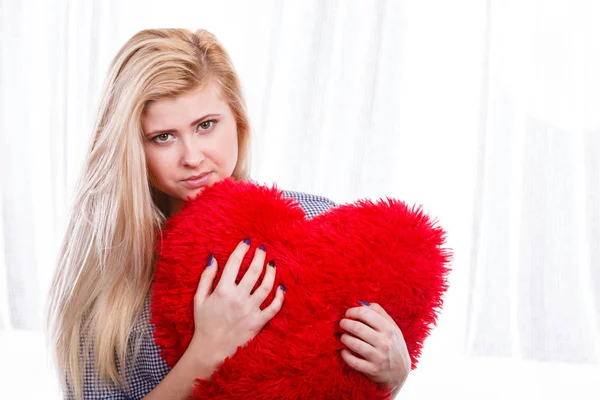 Sad woman holding red pillow in heart shape