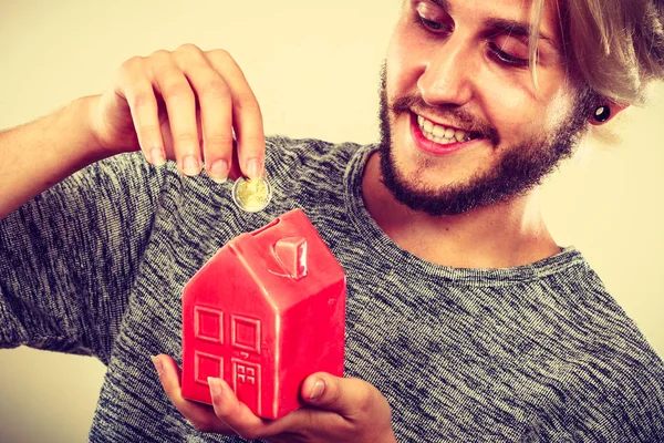 Χαμογελαστός άνθρωπος βάζοντας κέρμα στον κουμπαρά του σπιτιού — Φωτογραφία Αρχείου