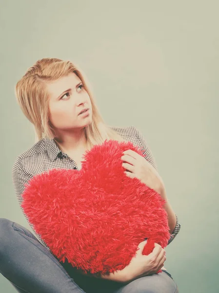 Traurige Frau mit rotem Kissen in Herzform Stockbild