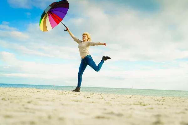 Woman jumping with colorful umbrella on beach — Stock Photo, Image