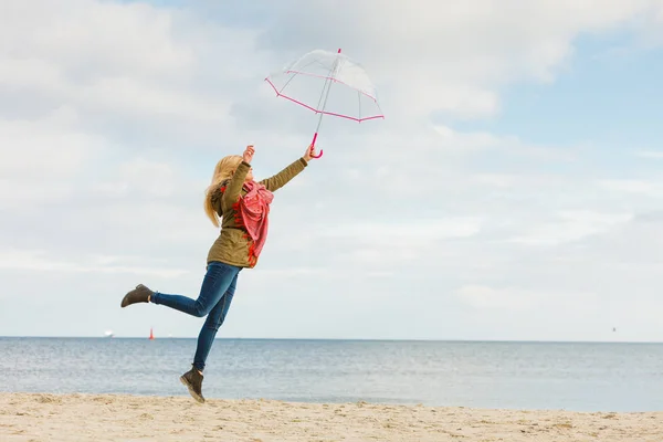 Kobieta, skoki z przezroczystym parasol na plaży — Zdjęcie stockowe