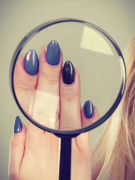 Woman looking at nails through magnifying glass Stock Picture