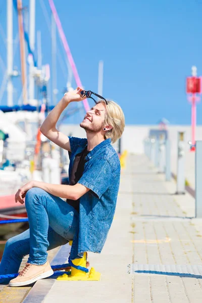 Blond człowiek siedzi w pobliżu portu w lecie — Zdjęcie stockowe