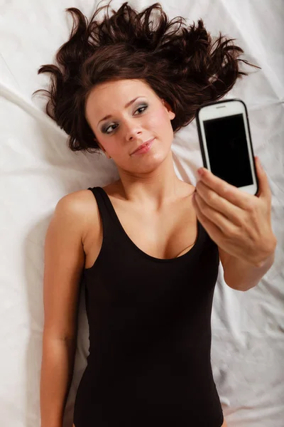 Sexy lazy girl lying with phone on bed in bedroom — Stock Photo, Image