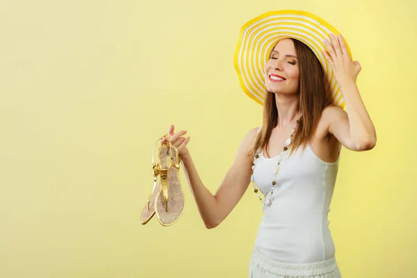 Kvinna i stora gula sommaren hatt innehar sandaler — Stockfoto