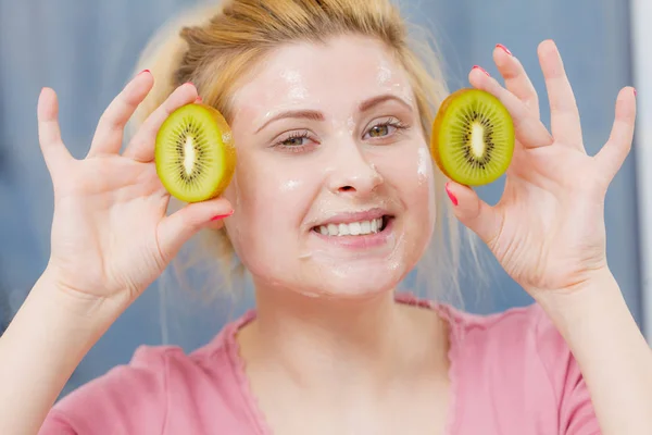 Vrouw met gel masker op het gezicht bedrijf kiwi — Stockfoto