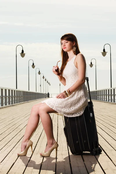 Woman sitting on suitcase, pier in background — Stock Photo, Image