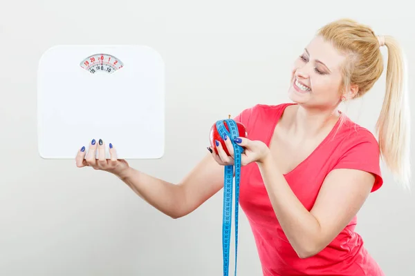 Woman holding apple,measuring tape and weight machine — Stock Photo, Image