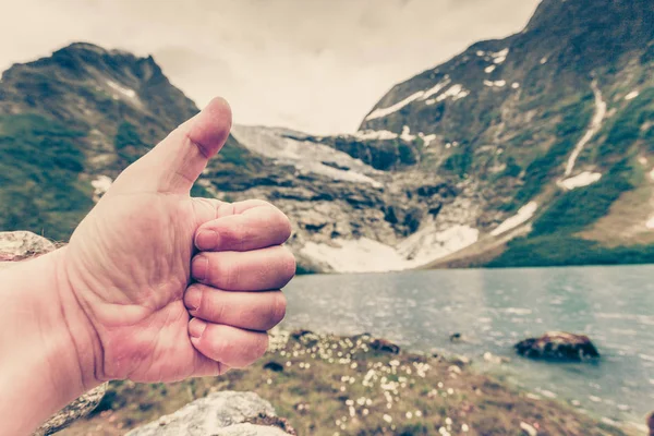 Male hand showing like with thumb up on mountains background
