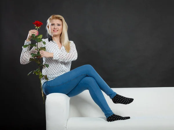 Дівчина сидить на дивані тримає червону троянду, на темряві . — стокове фото