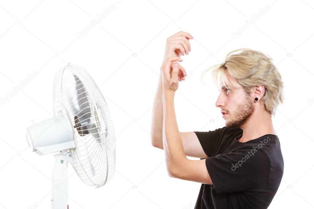 Young man fighting with wind from cooling fan