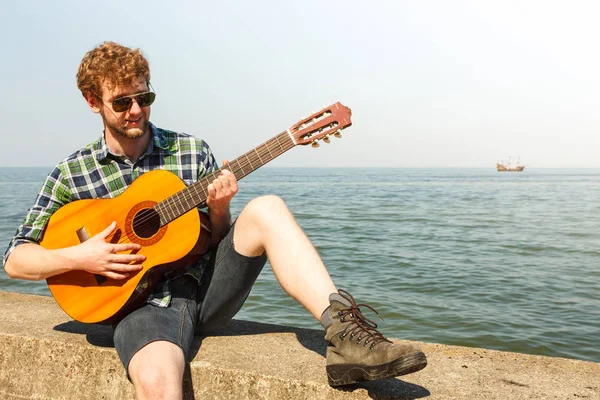 Giovane hipster suonare la chitarra dal mare oceano . — Foto Stock