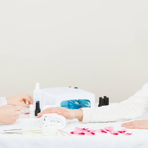 Close up of manicure beauty process. Smoothy hands of female beautician manicurist painting fingernails of woman using hybrid gel acrylic polish.