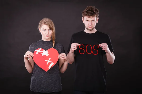 Young couple with broken heart and sos word.