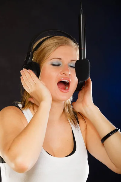 对在播音室里戴着耳机的麦克风唱歌的女人 — 图库照片