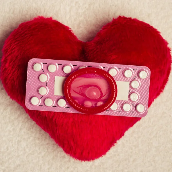 Píldoras anticonceptivas orales condón en el corazón rojo — Foto de Stock