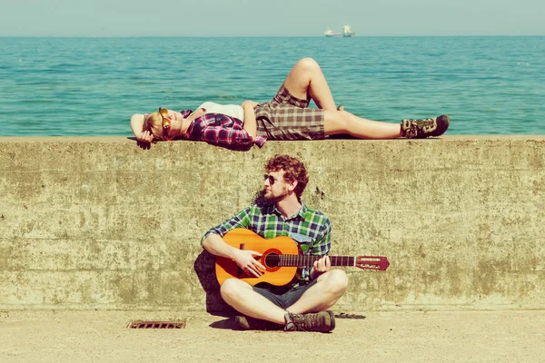 Młody mężczyzna gra na gitarze do jego dziewczyna nad morzem — Zdjęcie stockowe