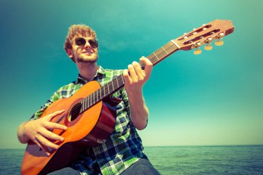 Deniz okyanus tarafından gitar çalmak hipster genç adam.