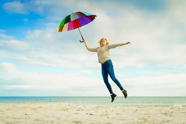 Vrouw springen met kleurrijke paraplu op strand — Stockfoto