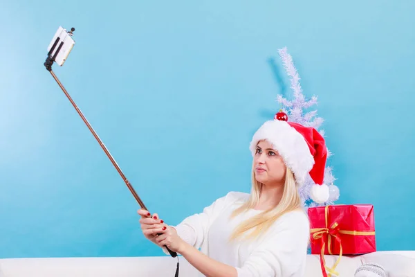 Girl in santa hat taking picture of herself using selfie stick — Stock Photo, Image